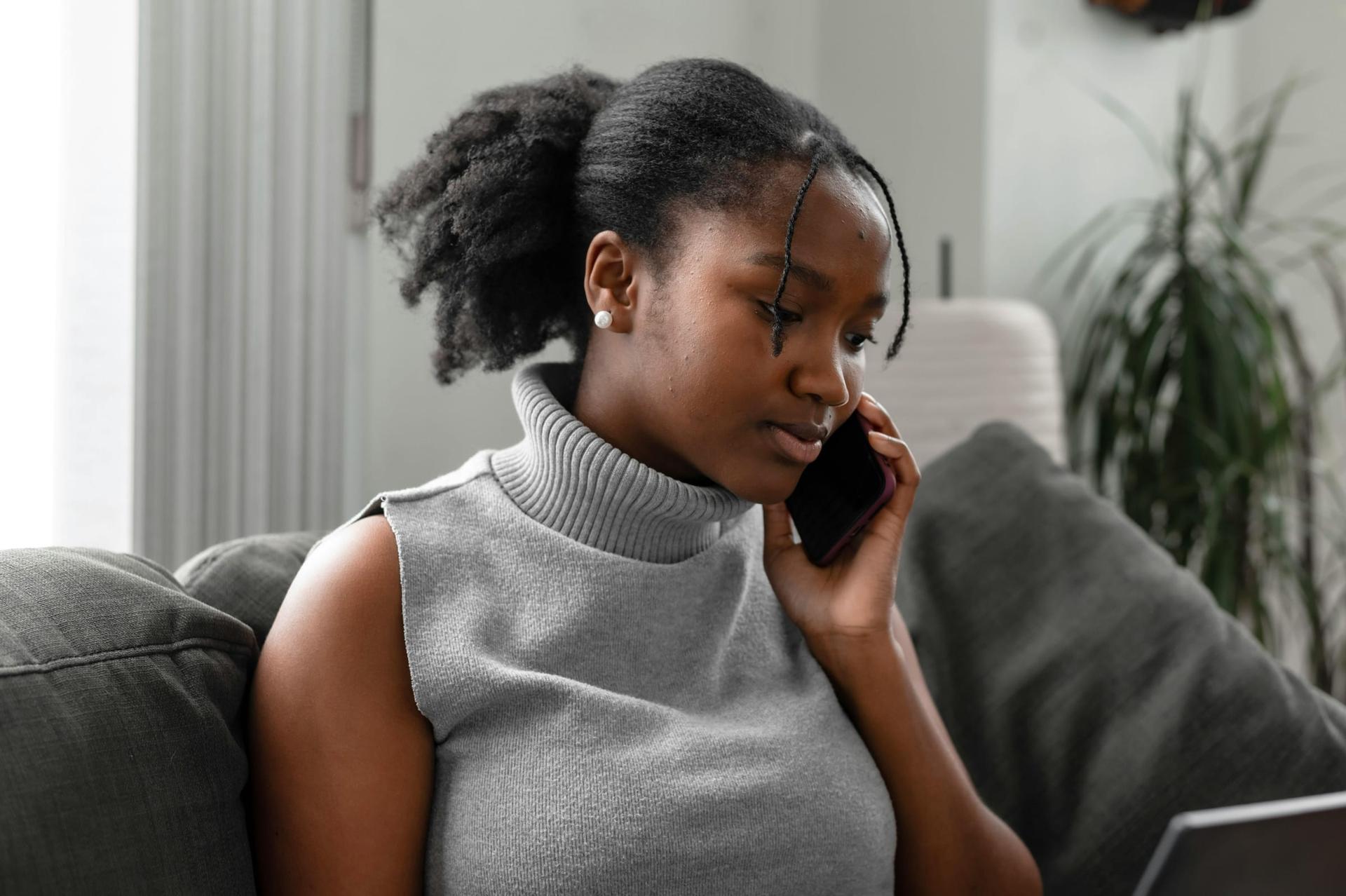 A woman in a grey turtleneck on a phone call from her sofa, listening.